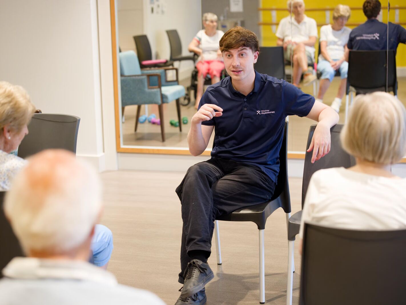 A physiotherapist seated with a small group of patients in a rehabilitation studio, talking with them.